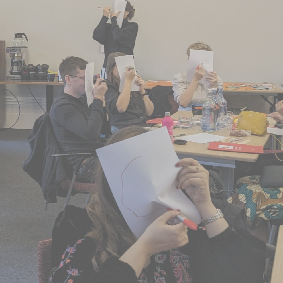 Participants in a workshop covering their face with paper and drawing their face on the paper without looking.
